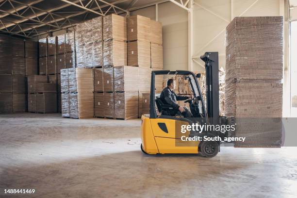 hombre conduciendo pilas de cartón en carretilla elevadora - carretilla elevadora fotografías e imágenes de stock