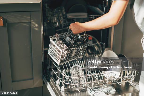 open dishwasher with clean utensils in it, man hands loading dishes to the dishwasher machine, introducing or taking out a plate and cup, clean tableware after cleaning process - dishwasher stockfoto's en -beelden