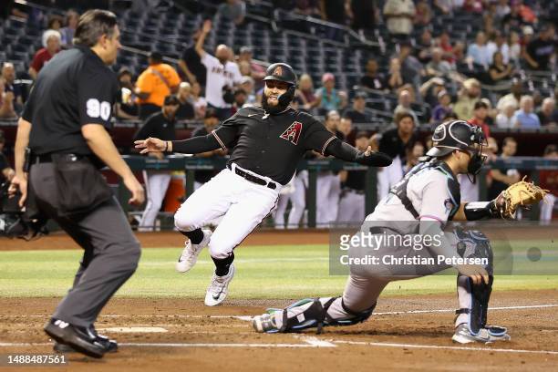 Emmanuel Rivera of the Arizona Diamondbacks slides into home plate to score a run past catcher Nick Fortes of the Miami Marlins during the fourth...