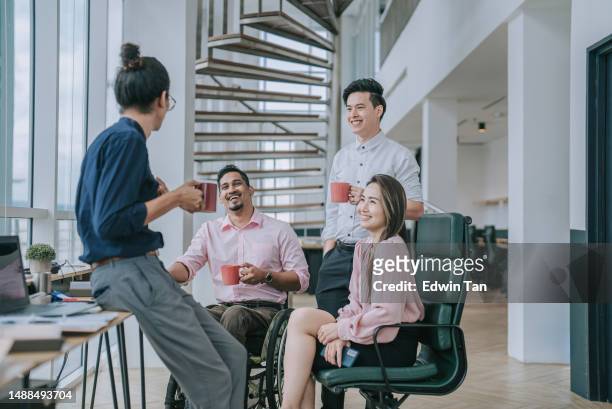 indian white collar male worker in wheelchair having cheerful discussion conversation with colleague in creative office workstation beside window - employee office happy stock pictures, royalty-free photos & images