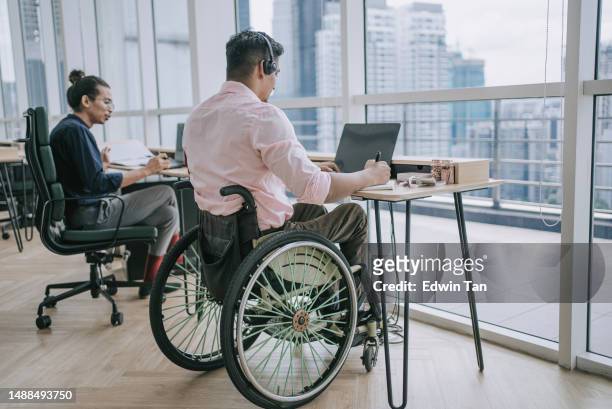 asian indian white collar male worker in wheelchair concentrating working in office beside his colleague - bring your own device stockfoto's en -beelden