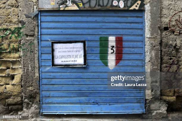 Blue colored gate with a graffiti of a shield and an ironic funeral poster with the inscription 'La capolista se ne va', the title of a famous chorus...