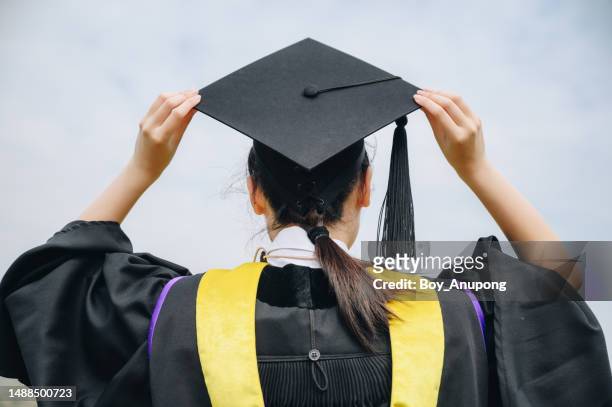 rear view of young student wearing graduation gown with graduation cap in her commencement day. - grad cap stock pictures, royalty-free photos & images
