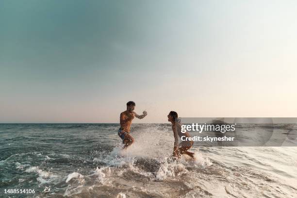 cheerful couple having fun while splashing each other at sea. - strand paar stockfoto's en -beelden