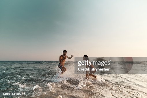 Cheerful couple having fun while splashing each other at sea.