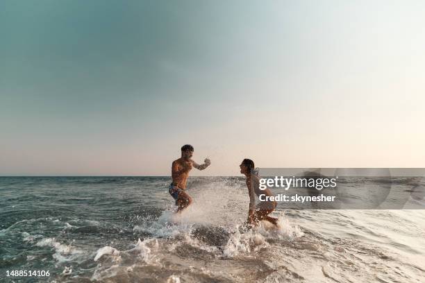 cheerful couple having fun while splashing each other at sea. - strand stock pictures, royalty-free photos & images