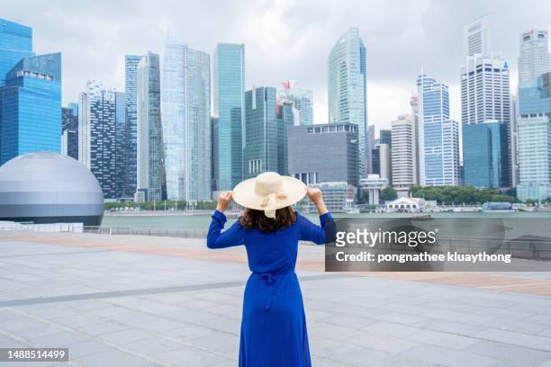 woman in blue dress wearing a hat stand and enjoy the view at marina bay in singapore - marina bay - singapore stock pictures, royalty-free photos & images