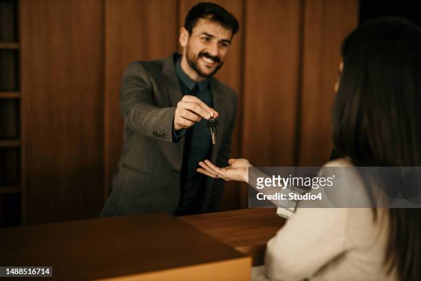 male receptionist talking with a hotel guest who is doing a check-in and giving her keys. - handing over keys stock pictures, royalty-free photos & images