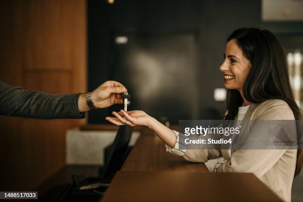 male receptionist talking with a hotel guest who is doing a check-in and giving her keys. - hotel key stock pictures, royalty-free photos & images