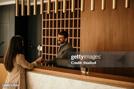 Smiling receptionist behind the hotel counter attending to a female guest. The concierge gives the documents to hotel guest. Smiling receptionist behind the hotel counter attending to a female guest. The concierge gives the documents to hotel guest.