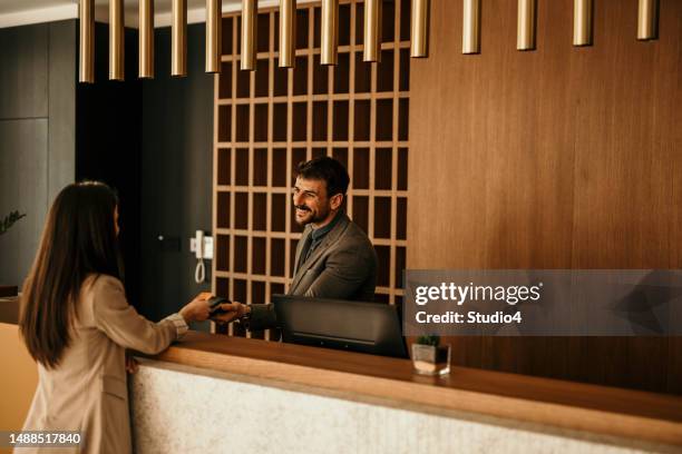 smiling receptionist behind the hotel counter attending to a female guest. the concierge gives the documents to hotel guest. - receptionist stock pictures, royalty-free photos & images