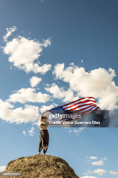 woman holding u.s. flag on july 4, holiday, cloudy blue sky, stand on rock with arms raised - american flag with one star stock pictures, royalty-free photos & images