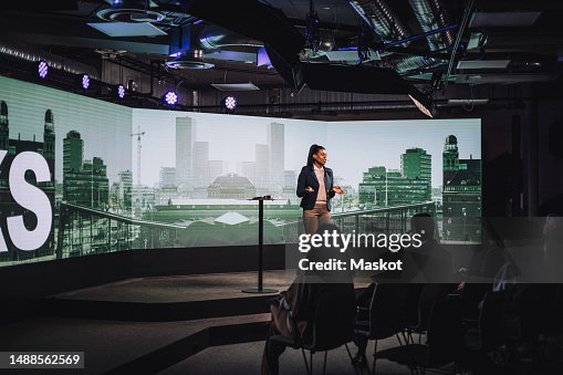 Female tech entrepreneur discussing with audience while standing on stage during tech event Female tech entrepreneur discussing with audience while standing on stage during tech event