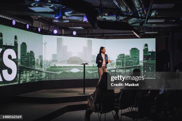 female tech entrepreneur discussing with audience while standing on stage during tech event - projection screen on stage stock pictures, royalty-free photos & images