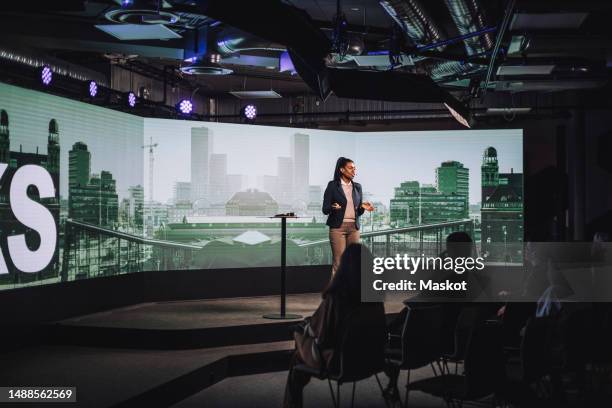 female tech entrepreneur discussing with audience while standing on stage during tech event - event speaker stock pictures, royalty-free photos & images