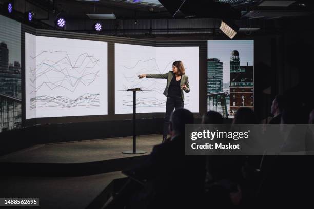 female public speaker explaining diagram to audience while standing on stage during tech event - pantalla de proyección fotografías e imágenes de stock