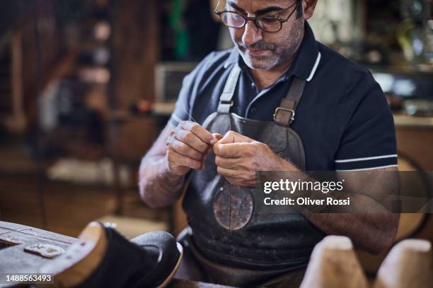 focused shoemaker at work in his workshop  with needle and thread - shoe repair stock-fotos und bilder