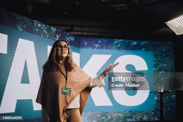 mature female tech entrepreneur standing and gesturing while giving speech at tech event - conference event stage stock pictures, royalty-free photos & images