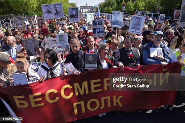 Russian-speaking people march from the Brandenburg Gate with portraits of Soviet soldiers who fought in World War II and a banner that reads: "the...