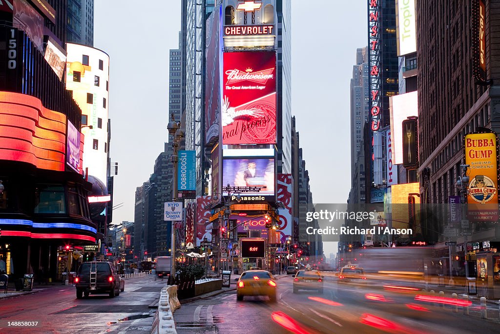 Traffic driving through Times Square at dusk.