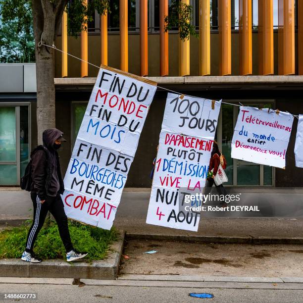 Un homme habillé en noir passe devant des slogans revendicatifs lors de la manifestation du 1er mai 2023 à Lyon.