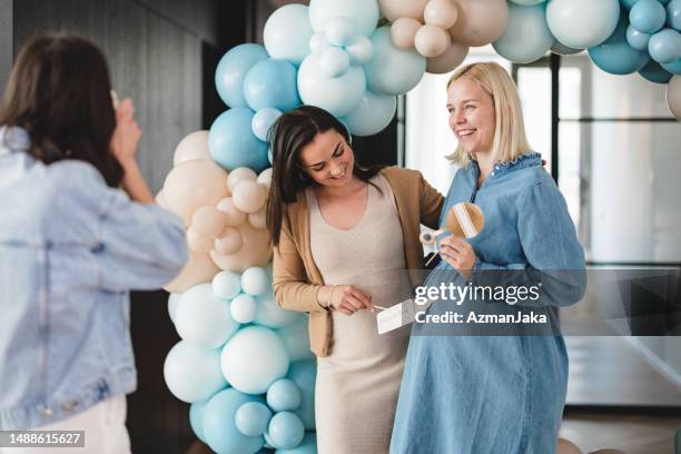 a group of female friends taking photos with a polaroid camera at a baby shower - balloon stomach stockfoto's en -beelden