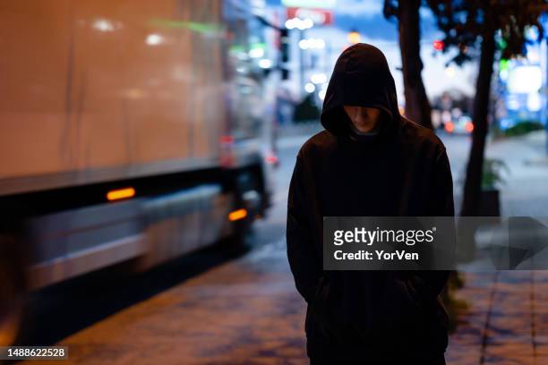 uomo senza volto con una felpa nera con cappuccio nella città della notte - uomo incappucciato foto e immagini stock