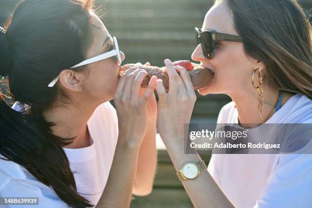 photo of two women sharing a pride-themed doughnut and embracing each other - friends donut stock pictures, royalty-free photos & images