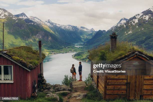 rückansicht eines paares, das ein malerisches bergtal mit alten holzhäusern in norwegen betrachtet - nordeuropa stock-fotos und bilder