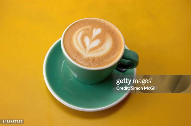 flat white coffee served in a green and white cup on a yellow table at an outdoor cafe - coffee heart fotografías e imágenes de stock