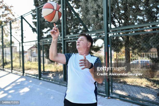 senior male spinning basketball and showing tricks - old basketball hoop stock pictures, royalty-free photos & images