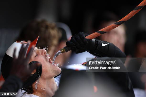Adley Rutschman of the Baltimore Orioles celebrates in the dugout with a water hose called the 'homer hose' after hitting a two run home run during...