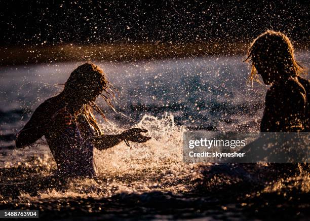 silhouette of a couple splashing each other in the sea. - ulcinj stock pictures, royalty-free photos & images