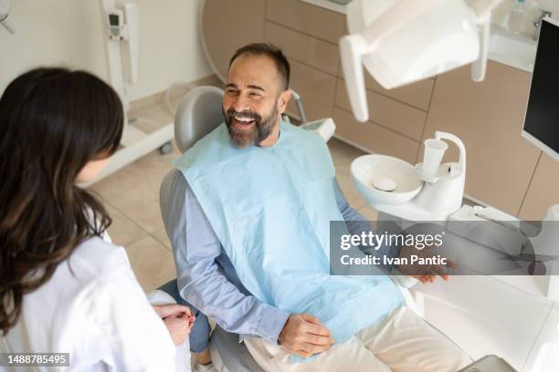 happy male patient talking to his dentist in medical clinic. - dental office stock pictures, royalty-free photos & images