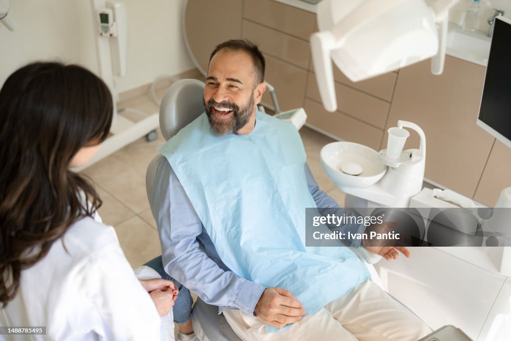Happy male patient talking to his dentist in medical clinic.