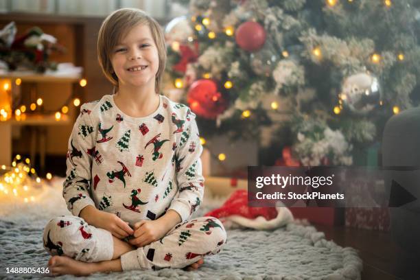 smiling boy sitting on the floor next to christmas tree - small child sitting on floor stockfoto's en -beelden