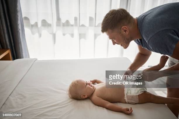 father changing diaper of baby girl lying on bed - diaper change stock-fotos und bilder