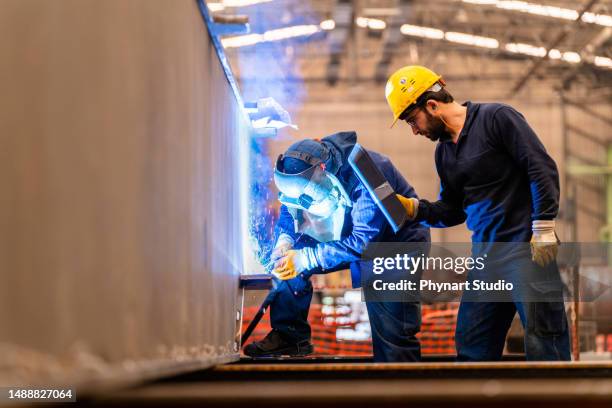 engineer teaching apprentice to use welding machine - metal workshop stockfoto's en -beelden