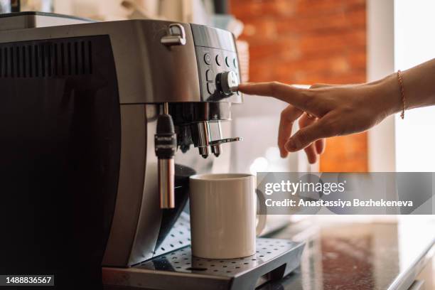 coffee machine with a white mug, a hand presses the buttons, home interior under the sun - automático imagens e fotografias de stock