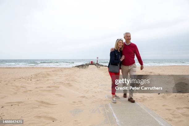 cheerful mature couple walking on a beach - mature men walking stock pictures, royalty-free photos & images