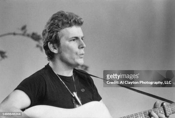 Musician singer songwriter Gordon Lightfoot shot waist up wearing a black tee shirt whistling and playing an acoustic guitar while rehearsing at the...