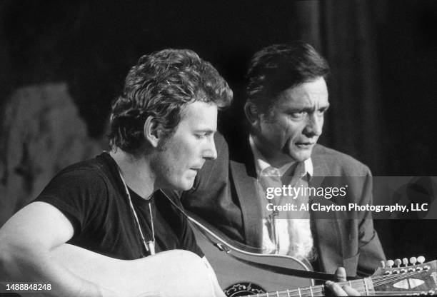 Musicians singer songwriters Gordon Lightfoot wearing a black tee shirt and Johnny Cash wearing a black suit with white shirt sitting on set playing...