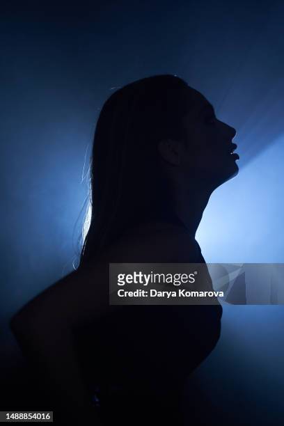 profile of a beautiful young woman in a black rock suit on a blue background on a stage in smoke. the portrait of a woman in shadow. the concept of a singer, a musician, a dancer on a stage. cover for your design with  copy space. - pride gradient stock pictures, royalty-free photos & images
