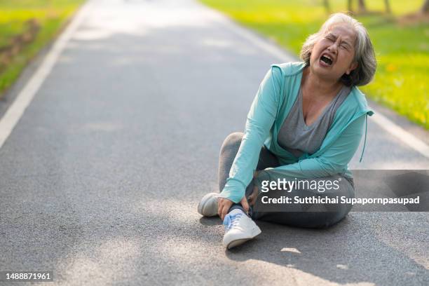 asian senior female getting pain at her leg  after slip and falling  while exercising in the park - frau in slip stock-fotos und bilder