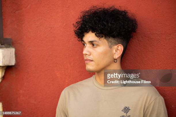 a young man leans against a wall and looks to his right side - hispanic man profile hopeful stock-fotos und bilder