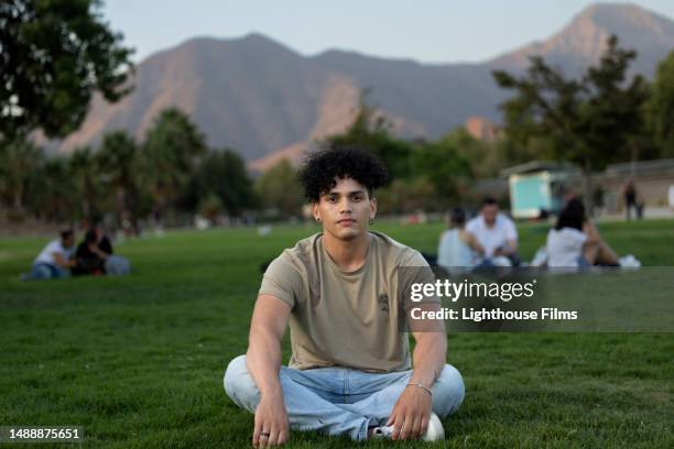 a man in front of a mountain range rests cross-legged on the grass - mann lässig gras sitzen stock-fotos und bilder