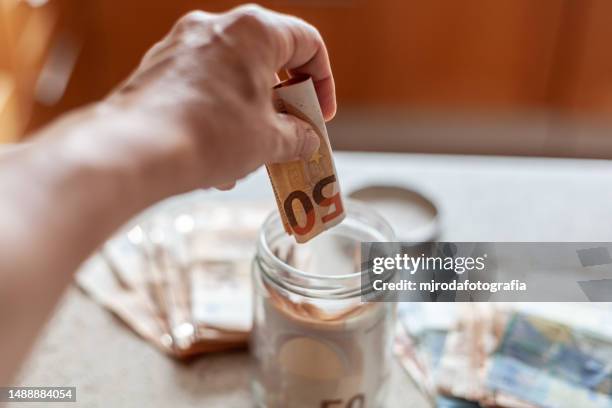 closeup of a hand keeping fifty euro bills in a glass jar - fajo de billetes de euro fotografías e imágenes de stock