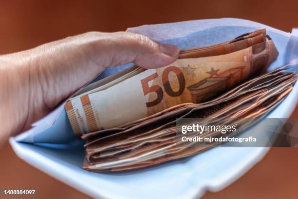 closeup of a hand holding a bunch of euro bills inside a white envelope - euro symbol stock pictures, royalty-free photos & images