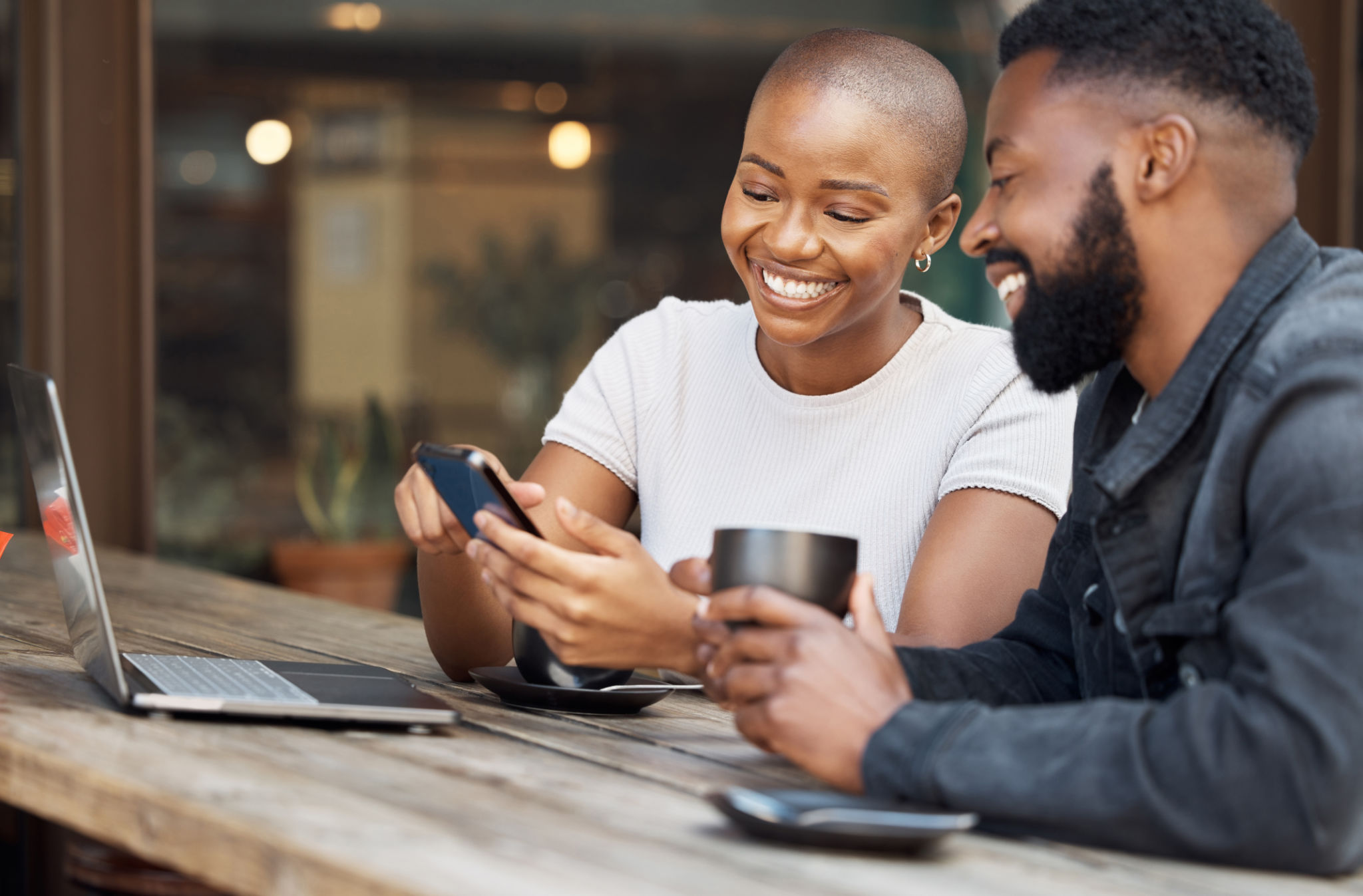 Cafe, social media and dating with a black couple laughing together at a table in a restaurant. Humor, love or date with a man and woman looking at a meme on a phone while bonding in a coffee shop Cafe, social media and dating with a black couple laughing together at a table in a restaurant. Humor, love or date with a man and woman looking at a meme on a phone while bonding in a coffee shop