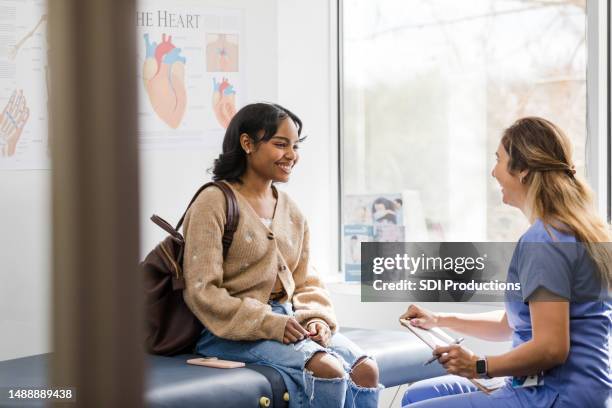 junge erwachsene patientin lächelt, während sie der krankenschwester zuhört, die ein ermutigendes update zu ihrer medizinischen untersuchung gibt - frauenarzt untersuchung stock-fotos und bilder